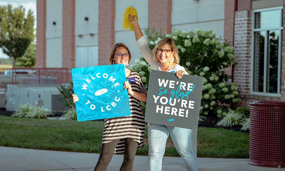 Two Women Holding LCBC Welcome Signs